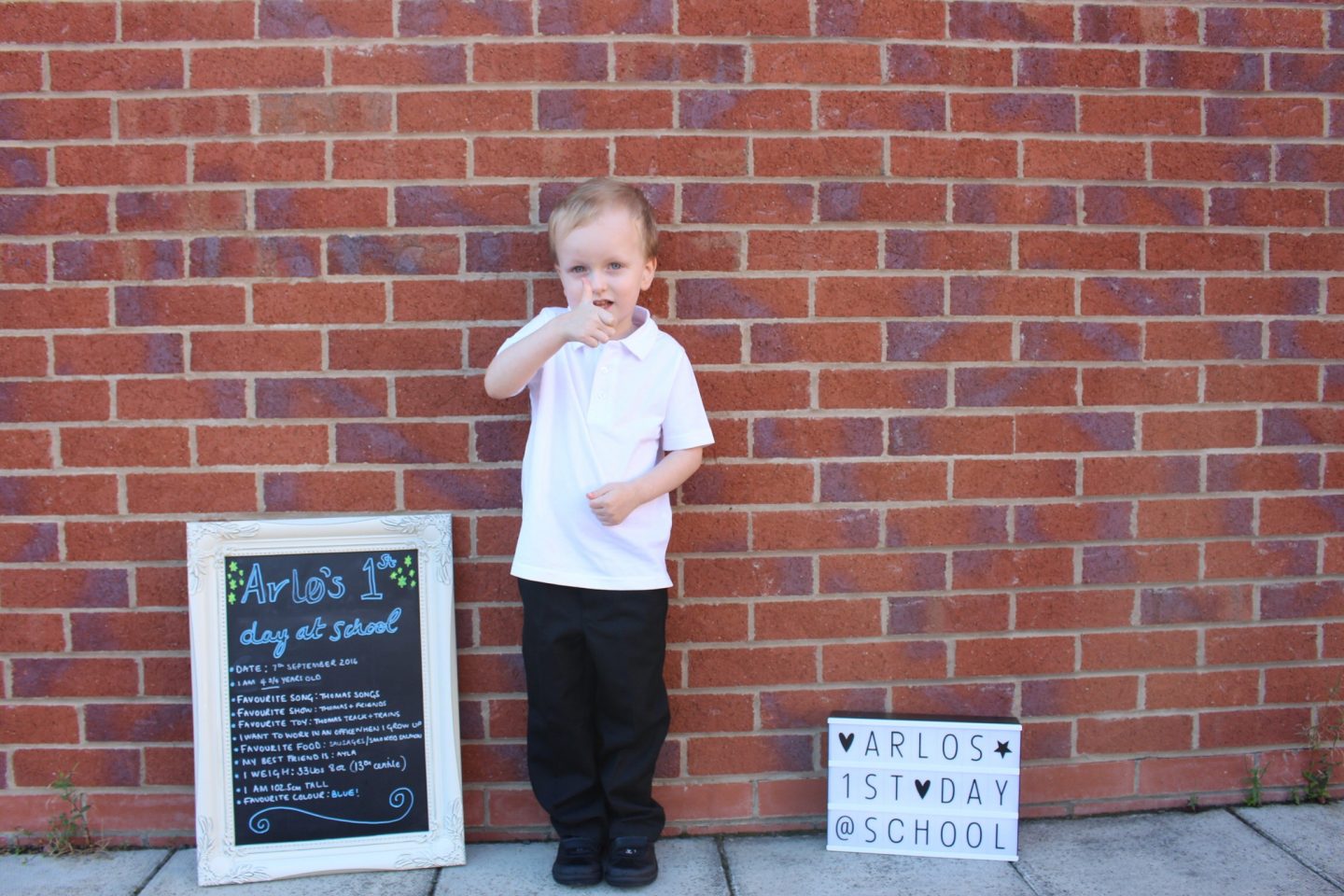 A little boy on his first day of school next to a sign that says 'Arlo's first day of school'