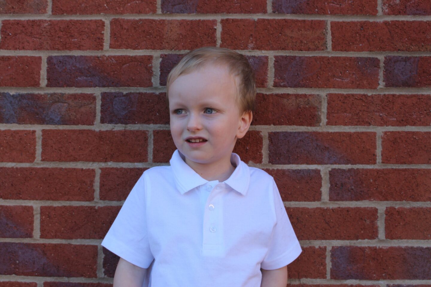 A 4 year old boy in his school top looking pensive