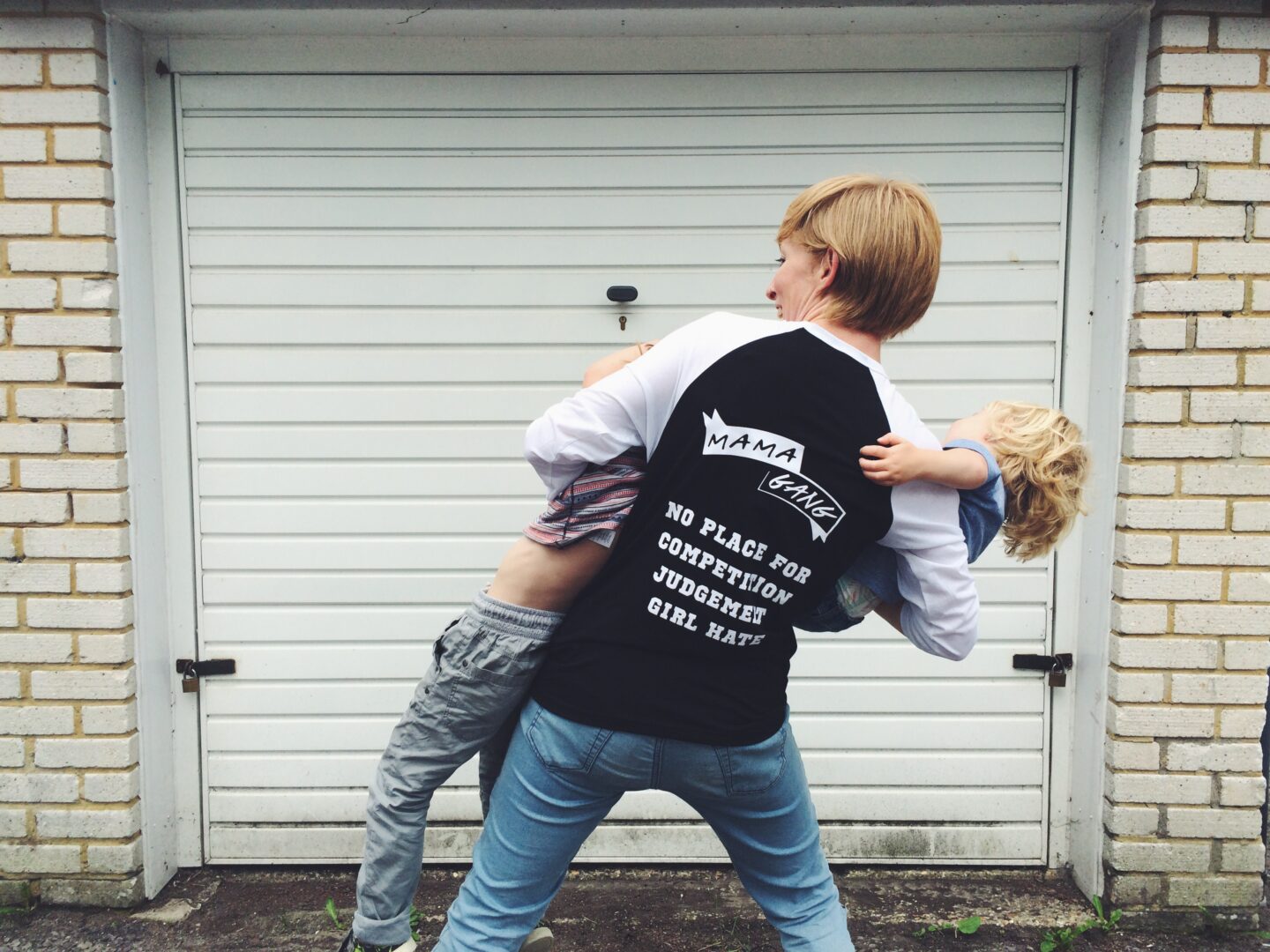 A blonde women carries two children, all their backs face the camera 