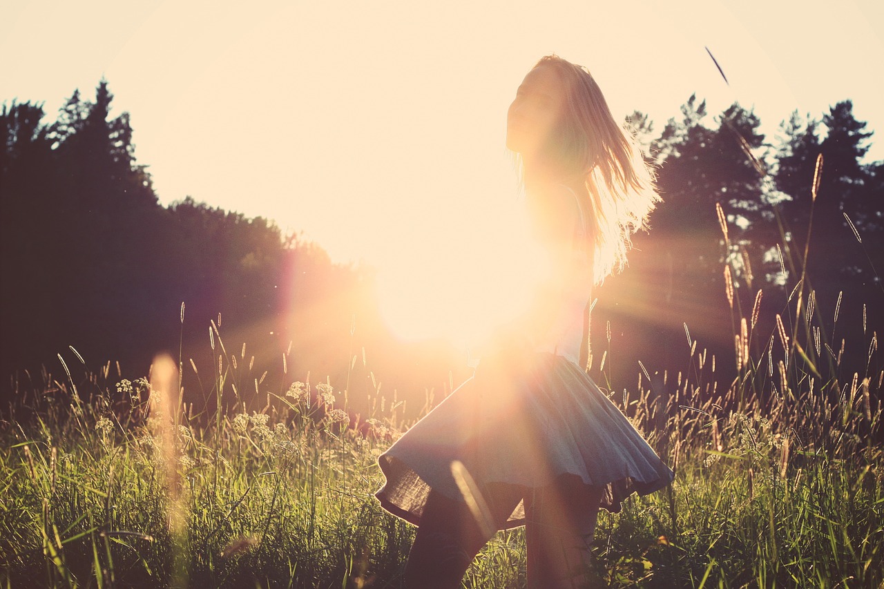 A girl twirls in a skirt in a field as the sun sets behind her