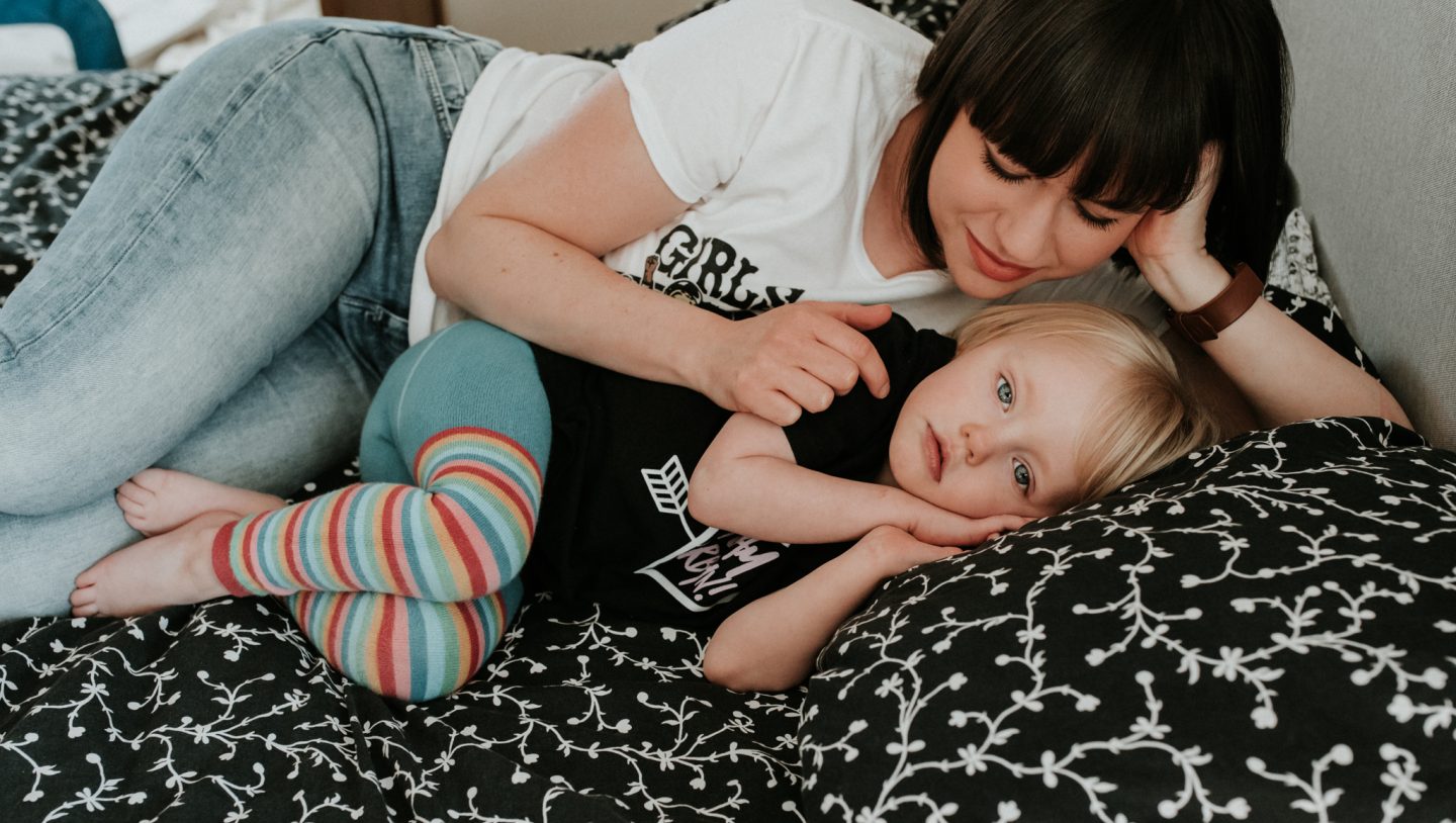 The ultimate guide to surviving when your kids don't sleep through the night - Nyomi and her daughter lay on the bed, Lena looking at the camera