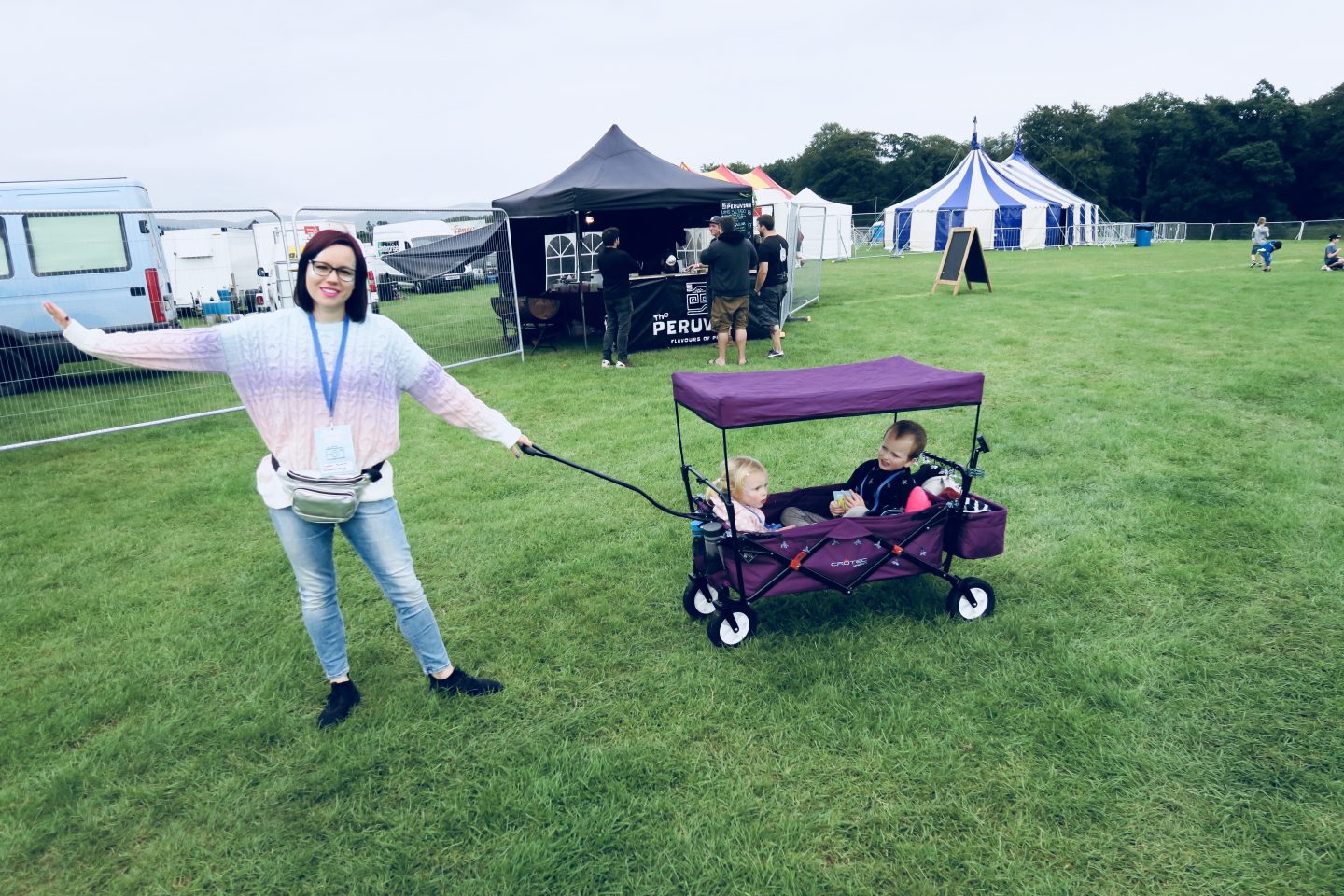 Woman pulling a wagon with kids inside it at a festival.