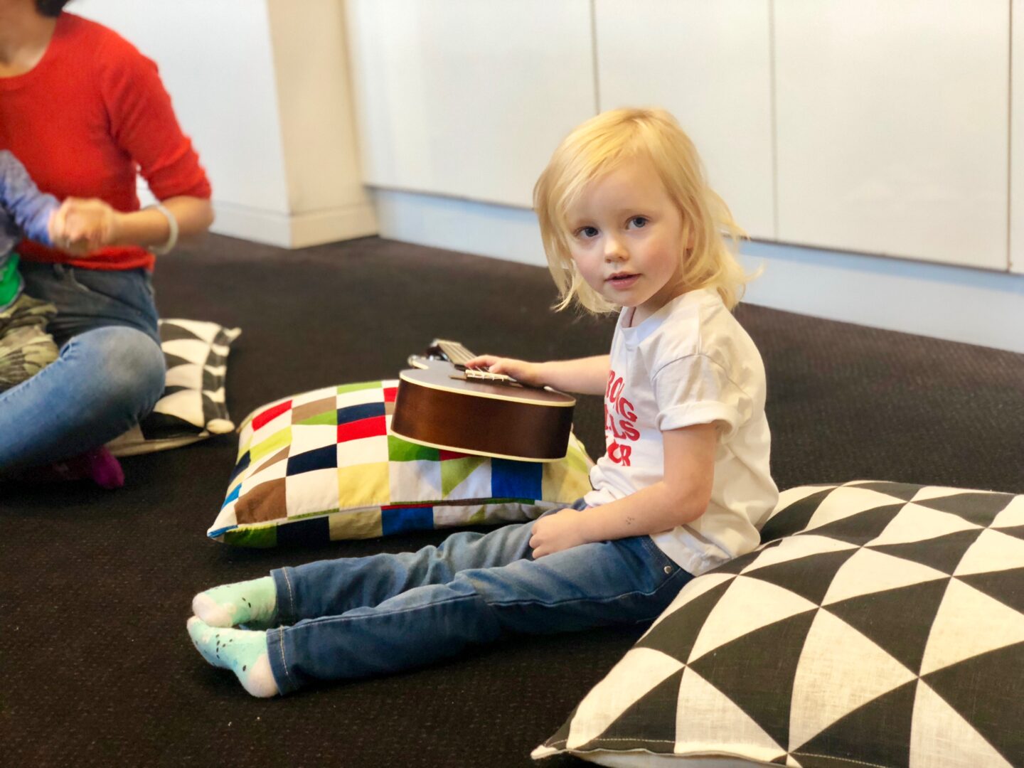 a 4 year old at a music playgroup smiling at the camera as she holds a ukulele. 