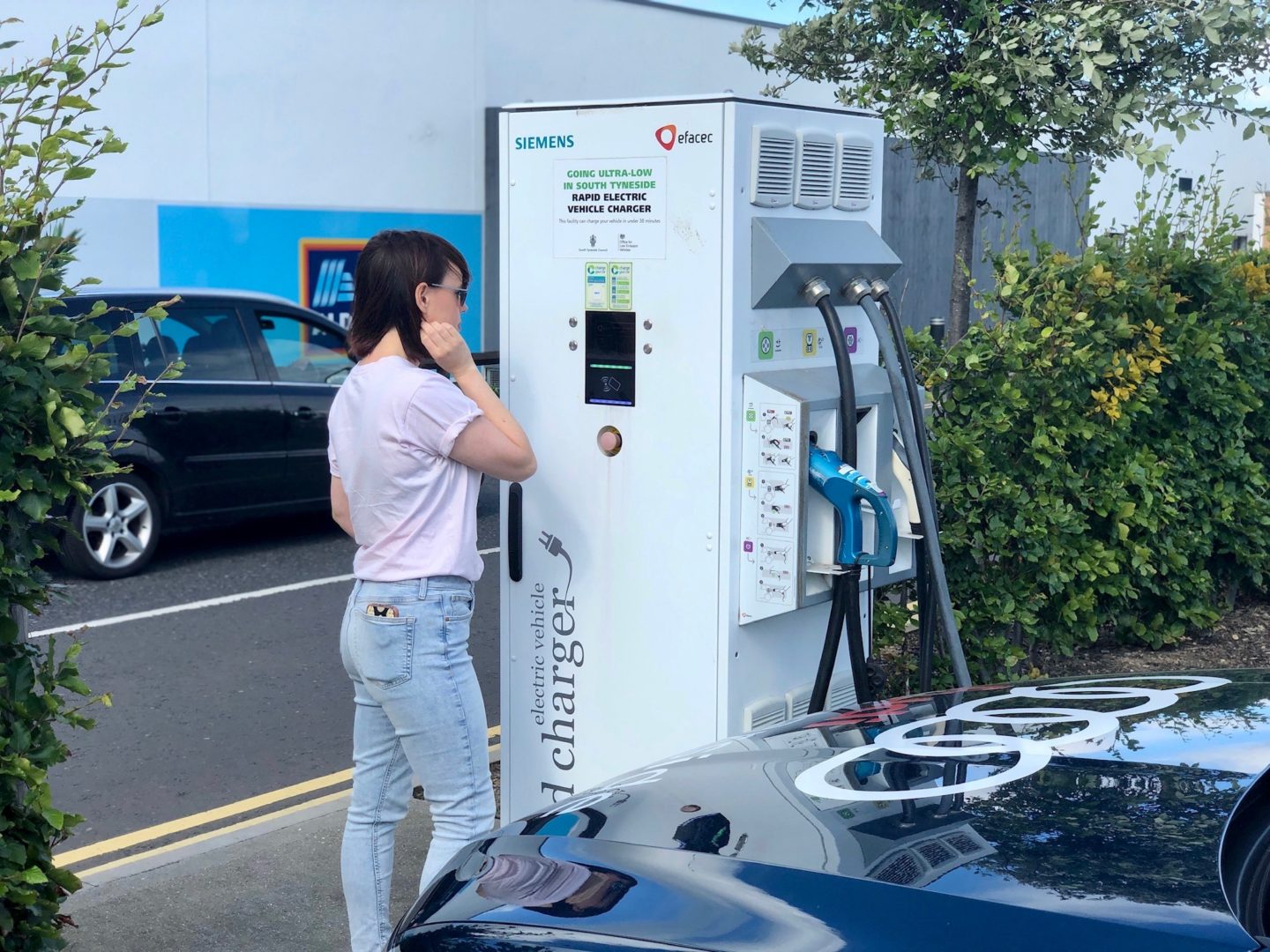 A woman looking at an electric vehicle charging point