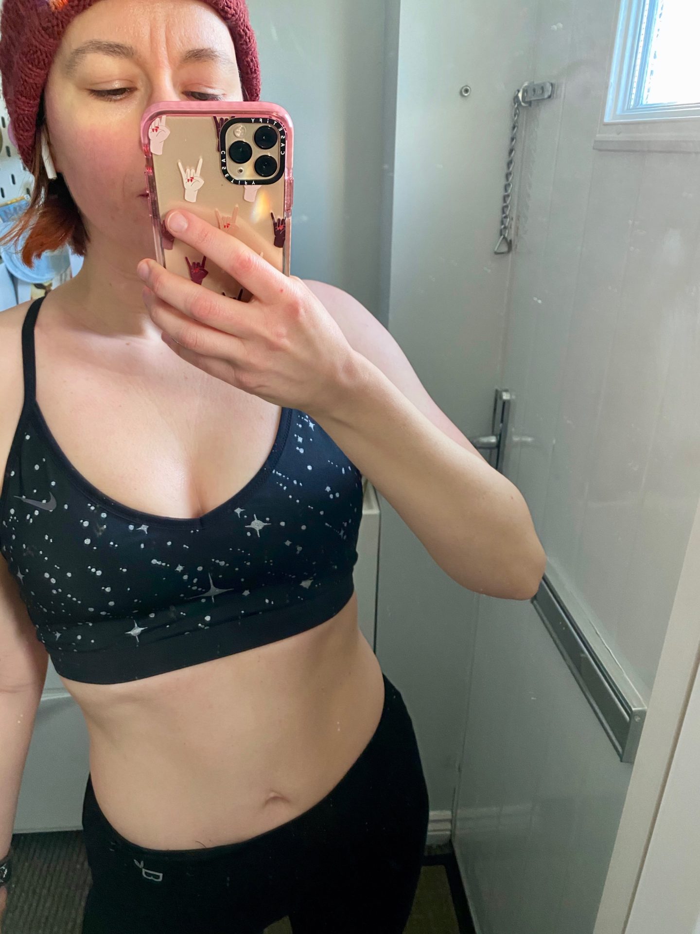 A woman in sports wear takes a selfie in a mirror, her abdomen is on display. 