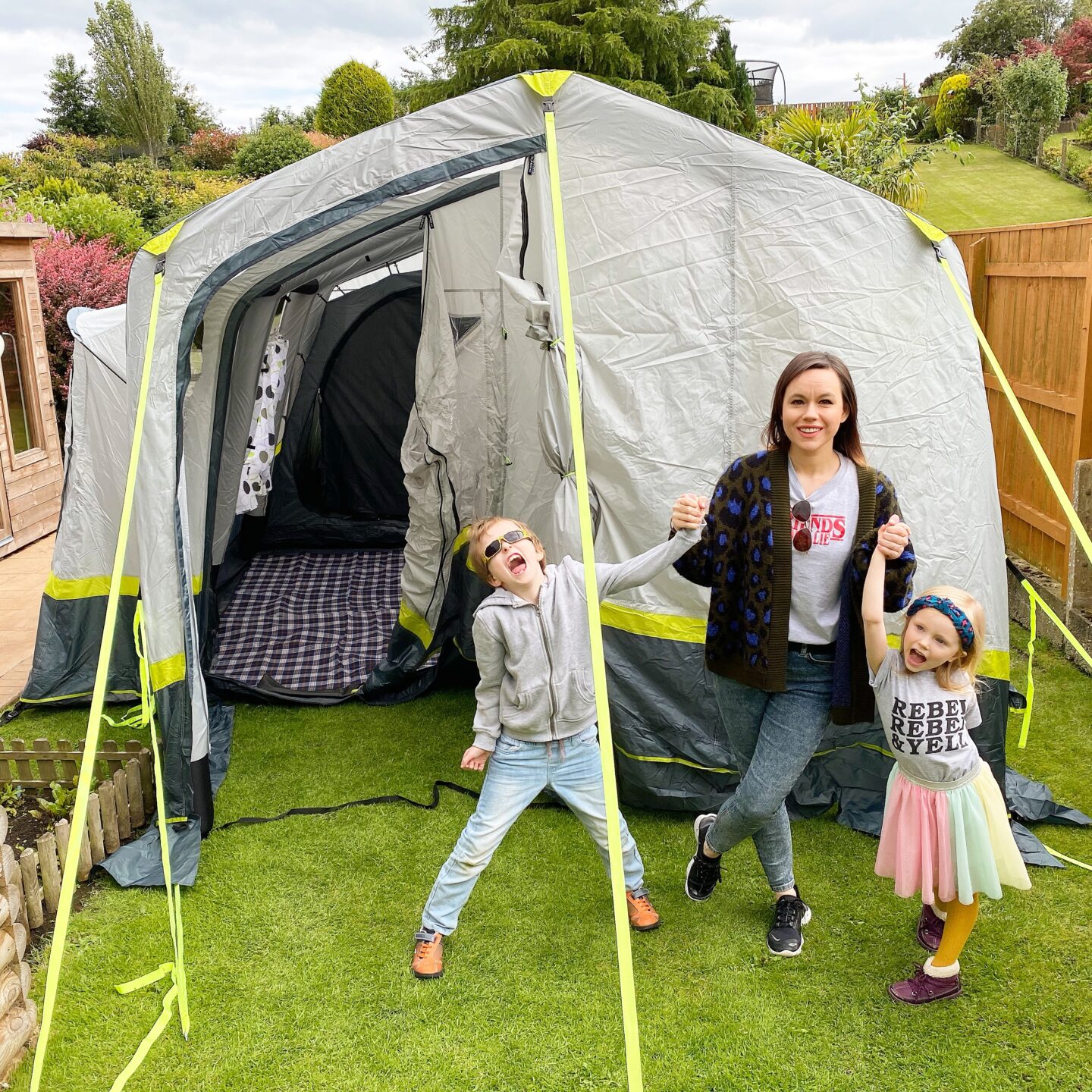 A mother and her son and daughter stand in from of ab OLPRO Home 5 birth family air tent looking happy and excited. 