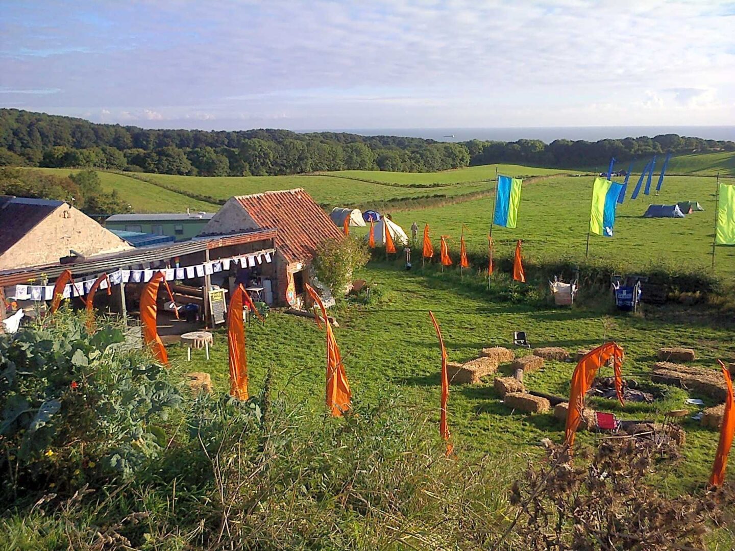 A farm and campsite with colourful flags overlooking the sea.