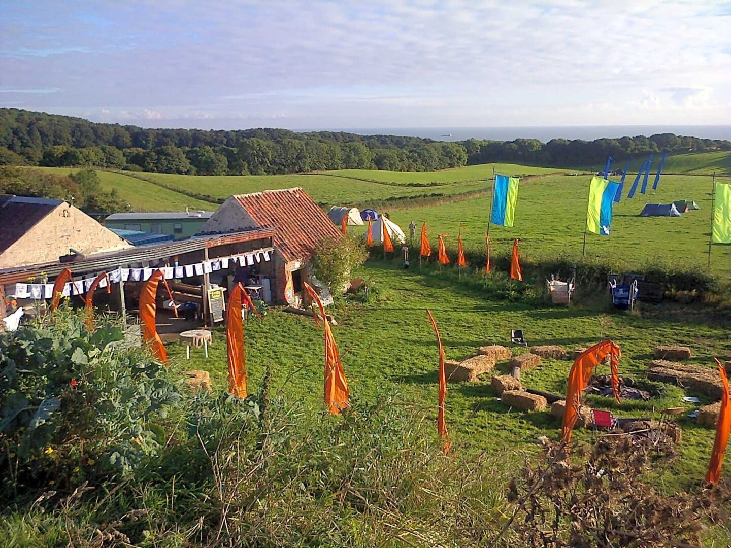 A farm and campsite with colourful flags overlooking the sea. 