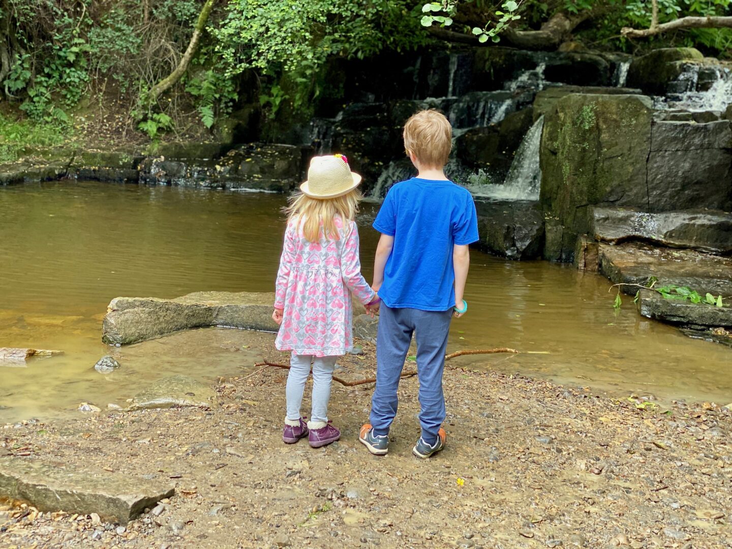 Two children holding hands looking at small waterfalls
