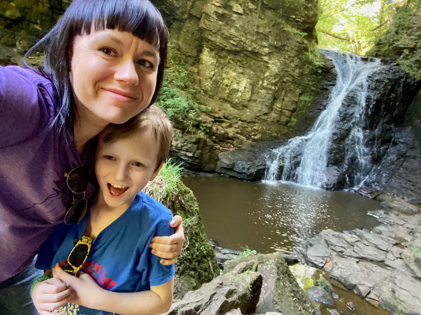 Woman and son stood smiling in front of a waterfall