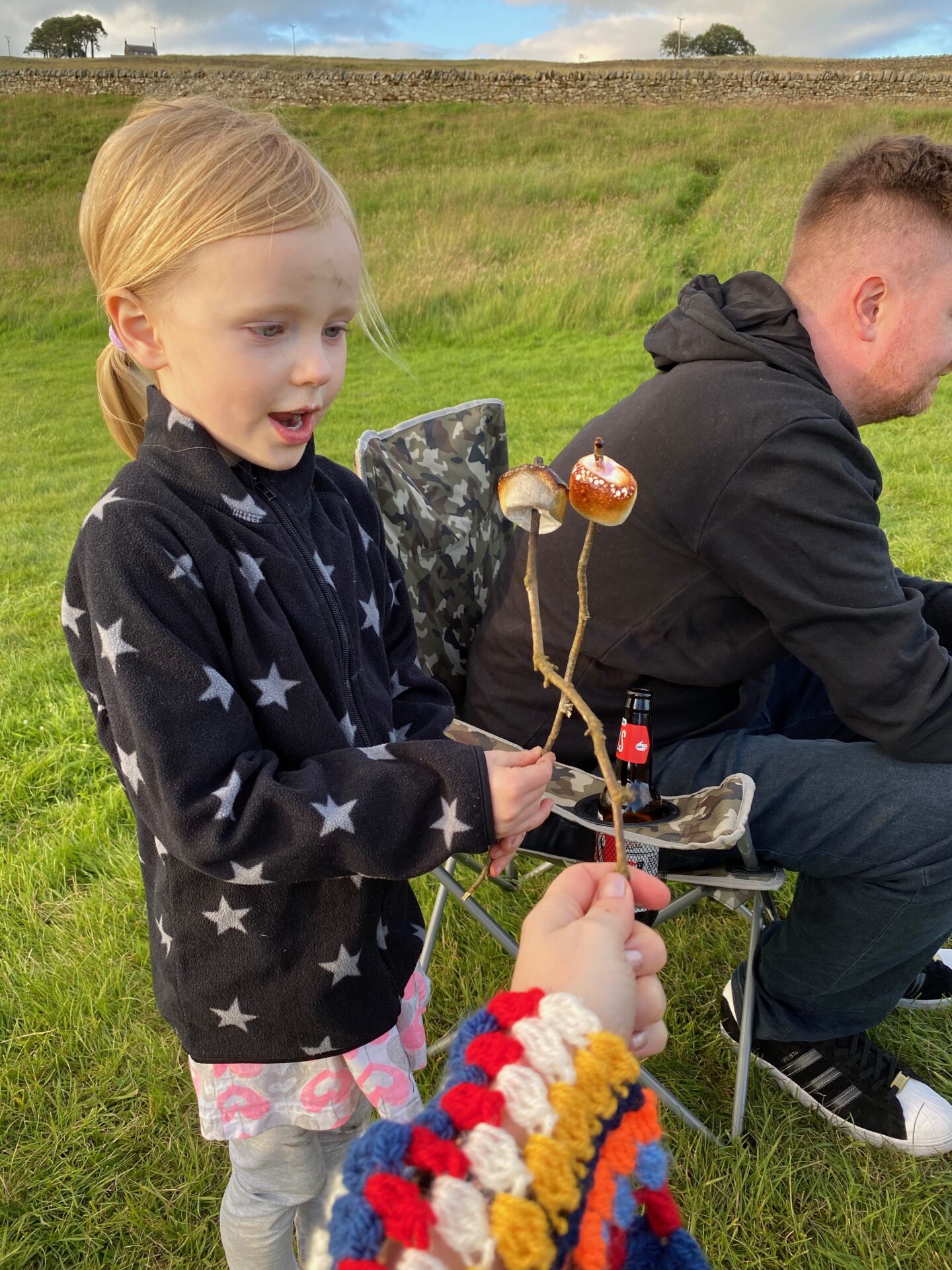 Little girl with blonde hair holding sticks with toasted marshmallows