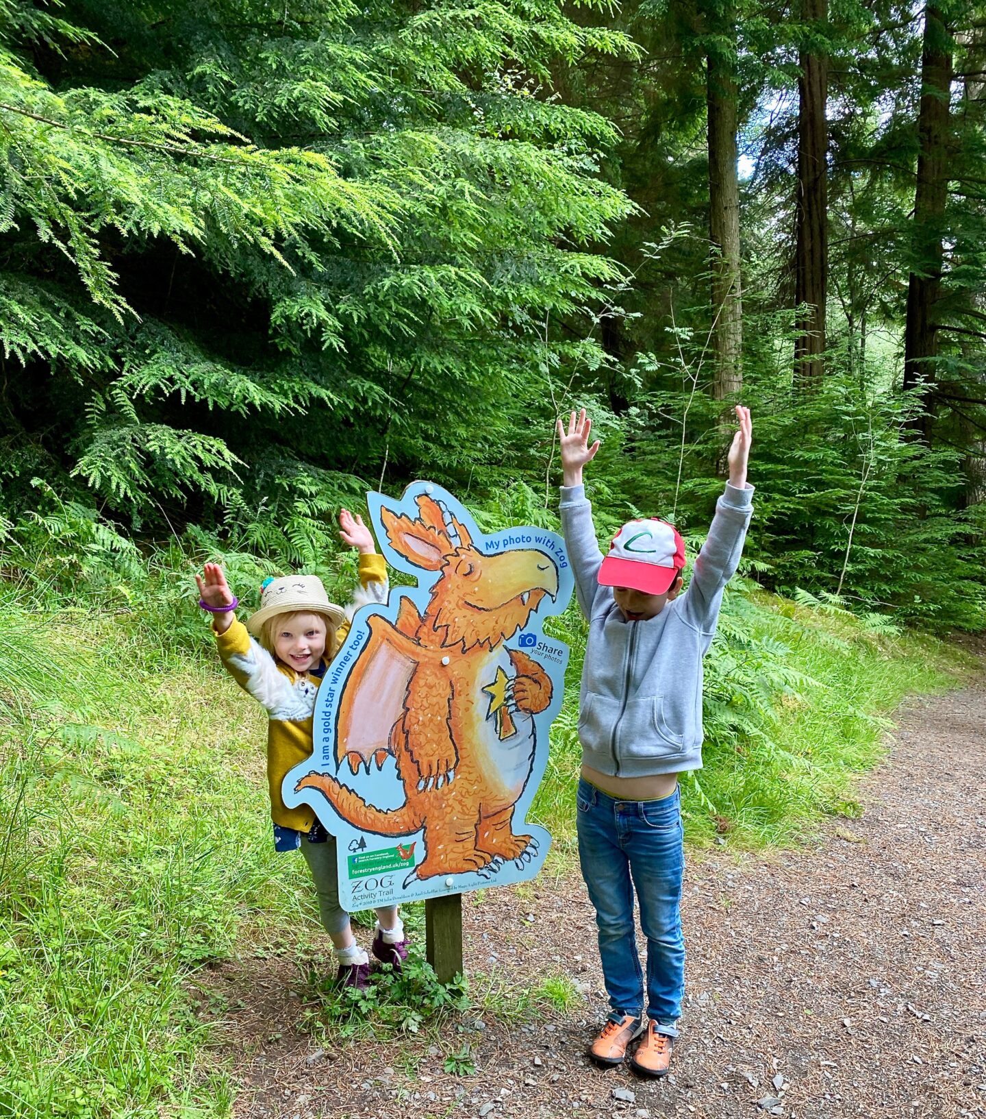 2 children holding their arms up in the air next to a Zog sign that makrs the end of a trail