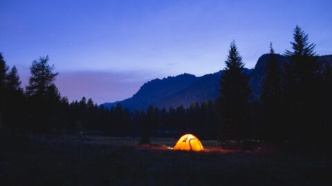 Tent glowing against the mountains during wild camping at night.