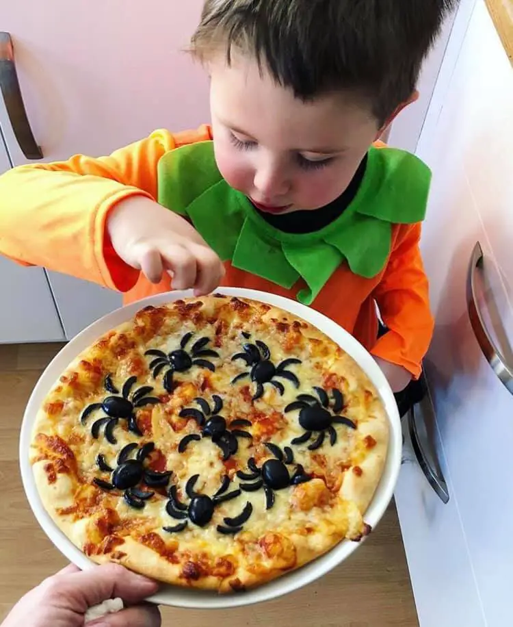 Boy with a pizza with spiders made from olives