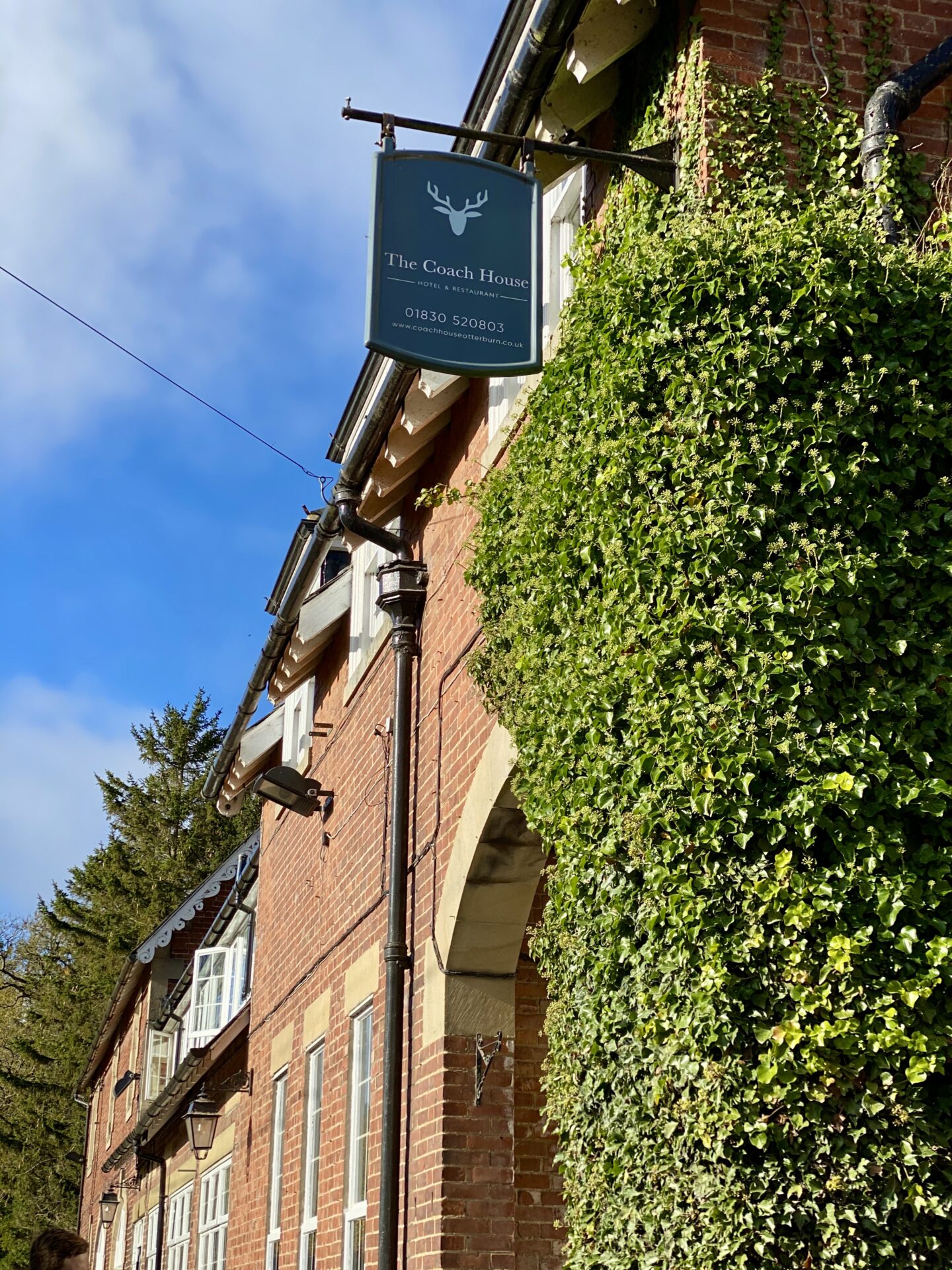 A photo of the exterior of a pub showing the Coach House sign and greenery