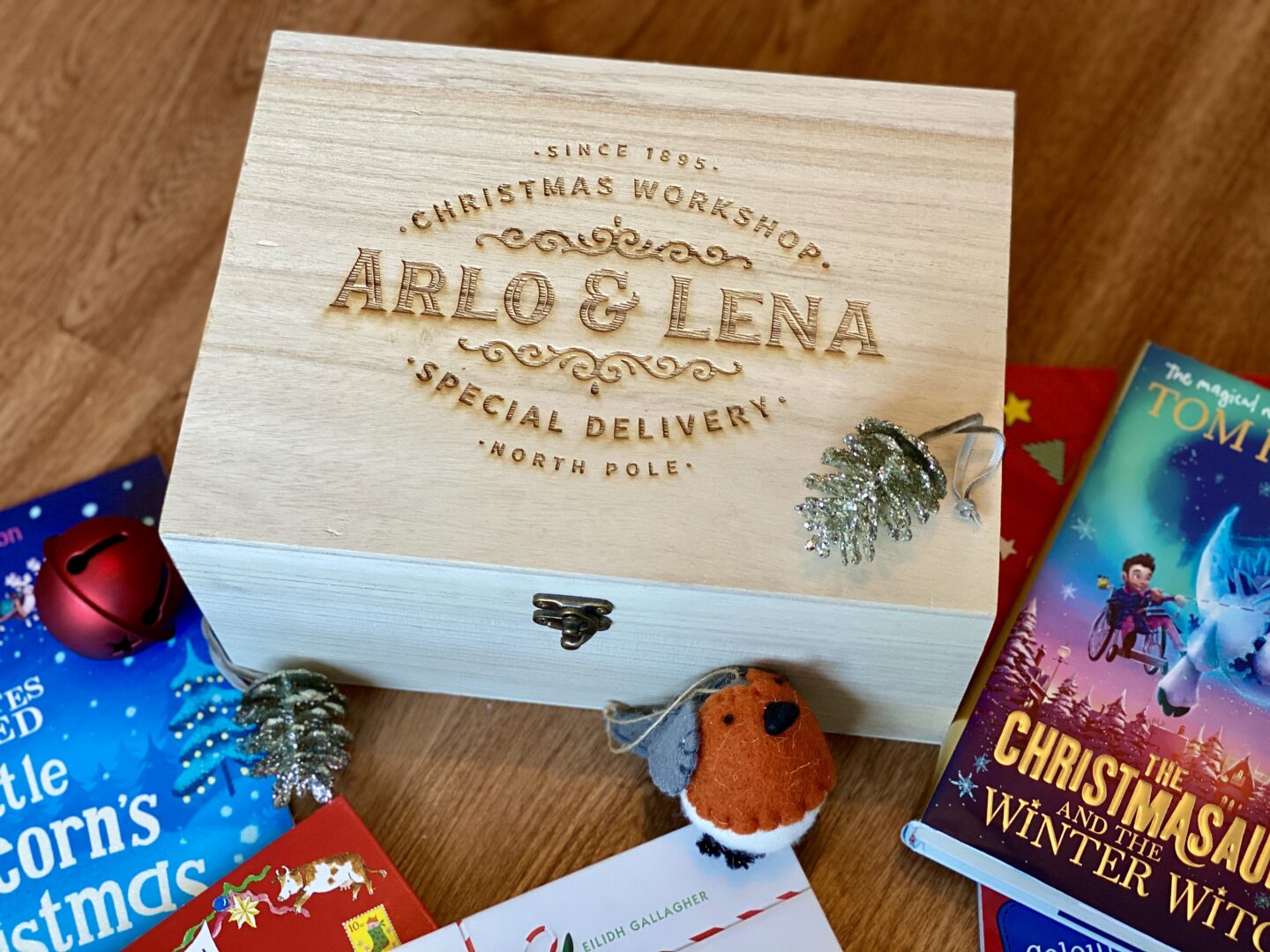 An engraved wooden Christmas tree day box that has the names to Arlo and Lena engraved in it. Surrounded by christmas books