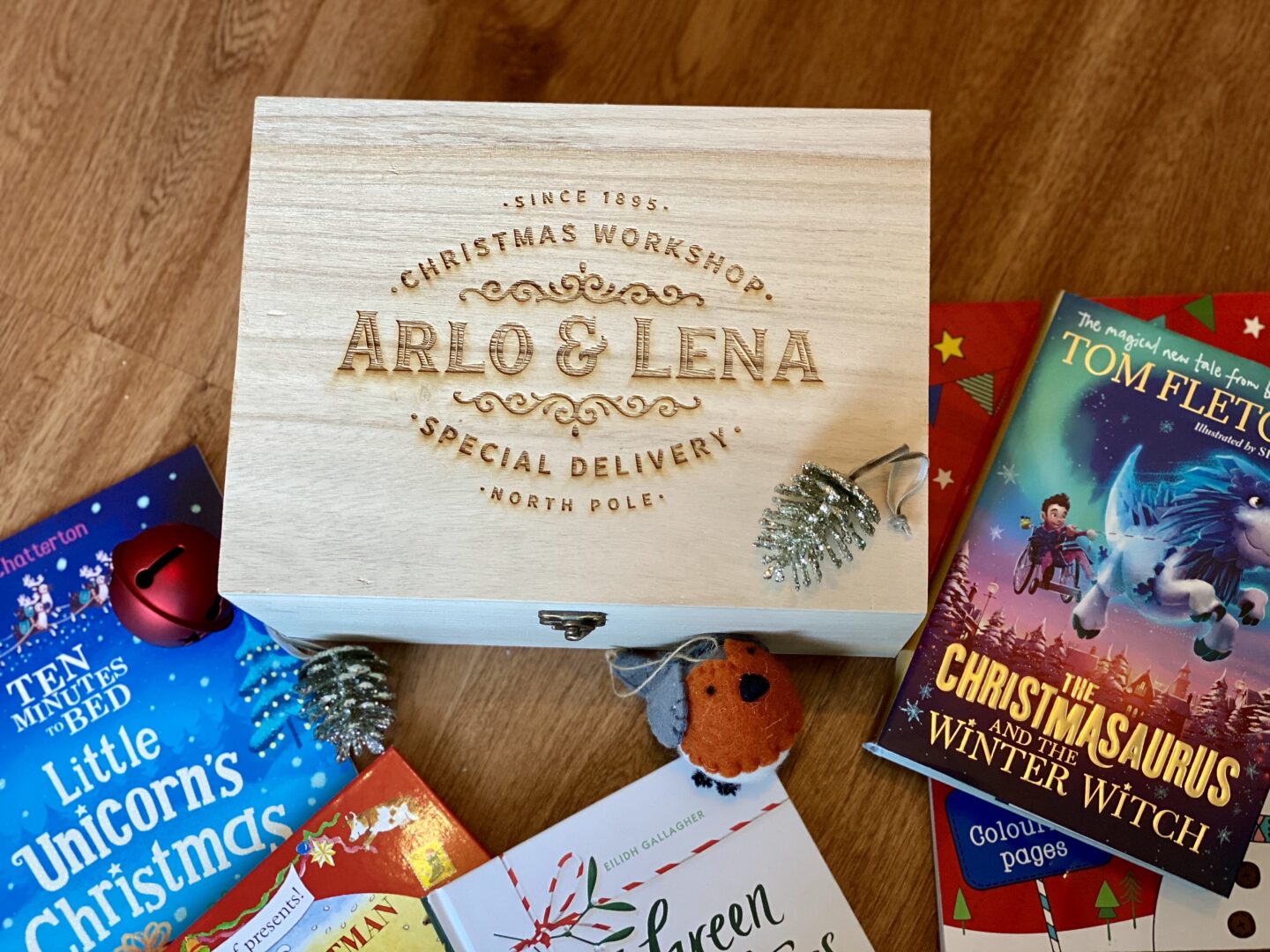 An engraved wooden Christmas tree day box that has the names to Arlo and Lena engraved in it. Surrounded by christmas books