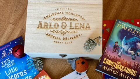 An engraved wooden Christmas tree day box that has the names to Arlo and Lena engraved in it. Surrounded by christmas books