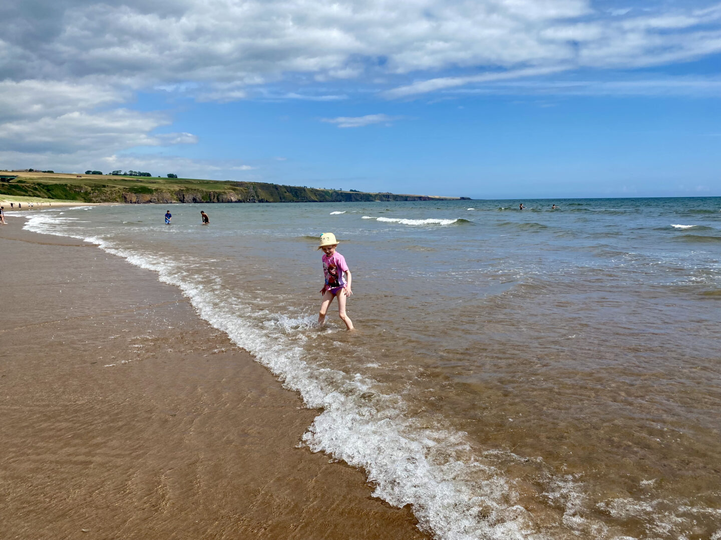 A little girl plays in the waves at Lunan Bay, Angus, Scotland