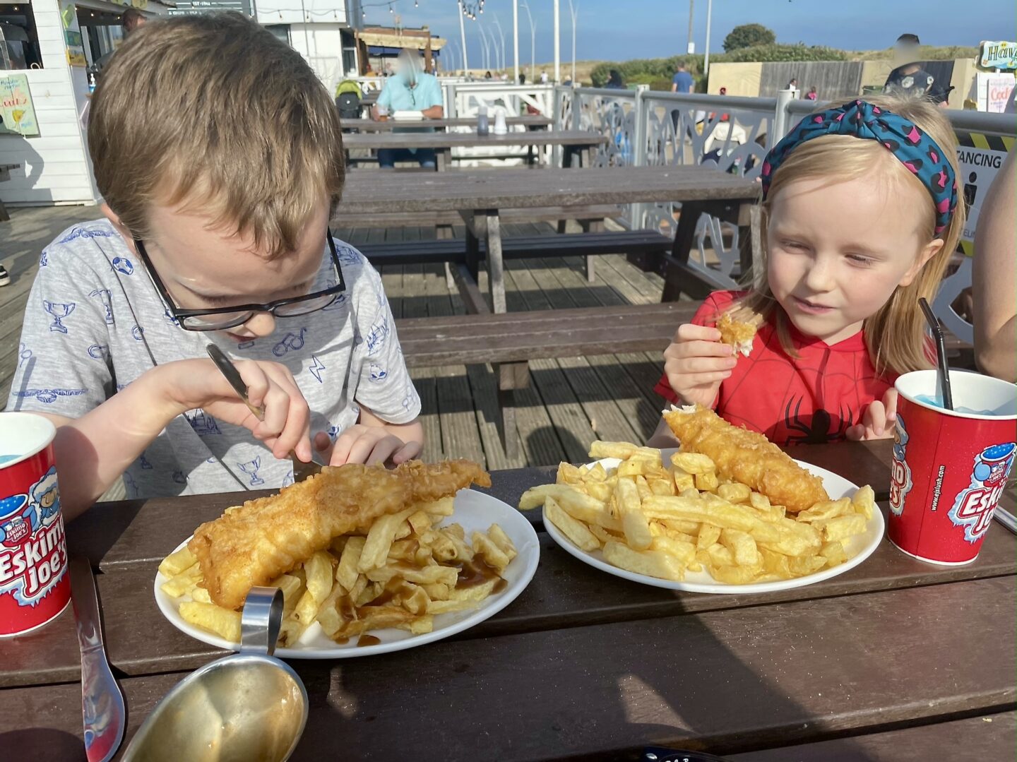 A boy and girl eat plates of fish and chips 