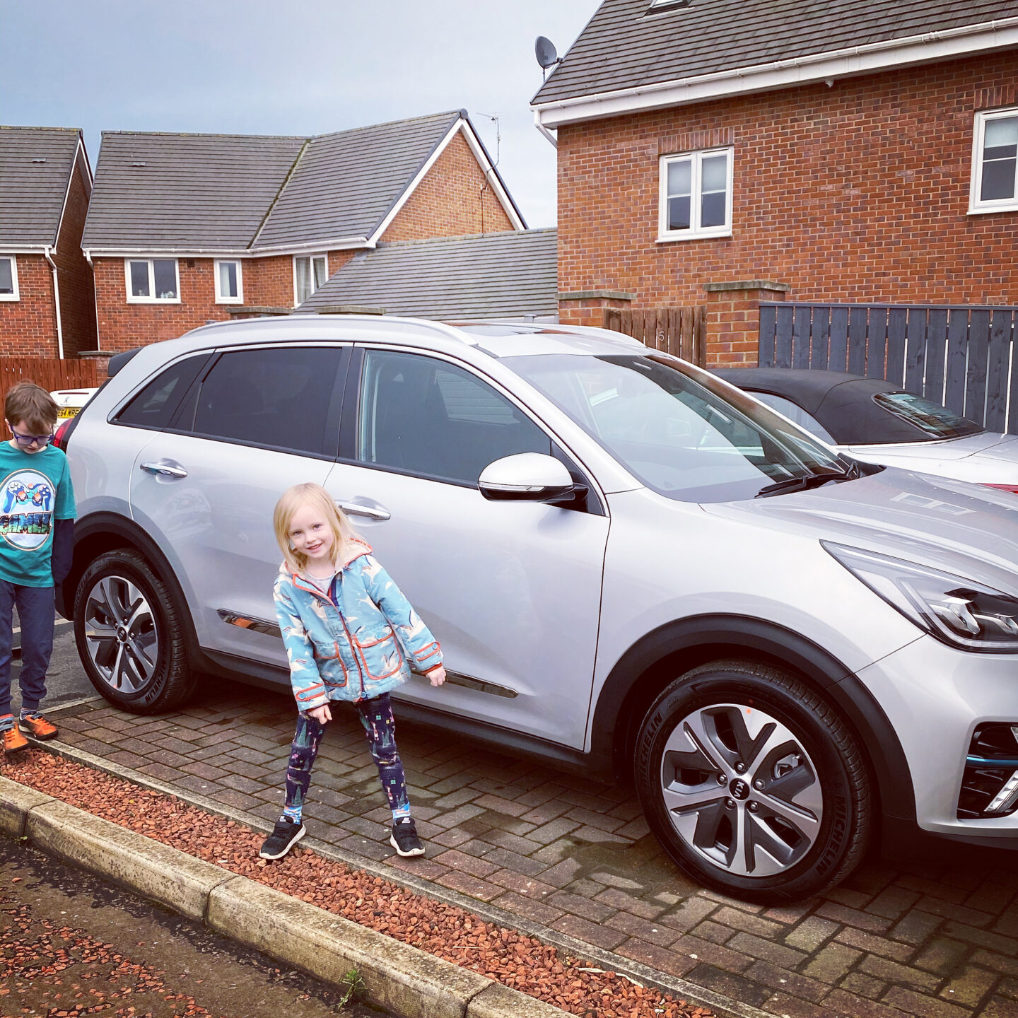 Children look happy around their new silver electric car