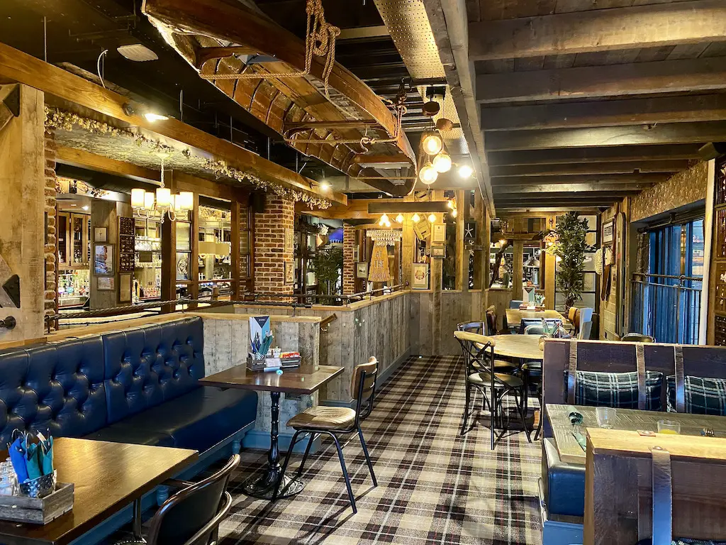 A dining room with wooden booths, blue and brown leather, checked carpets and an upside down wooden boat hanging from the ceiling.