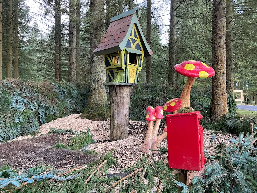 Giant brightly coloured wooden toadstools, a red post box and a little house on a tree stump in the middle of the forest. 