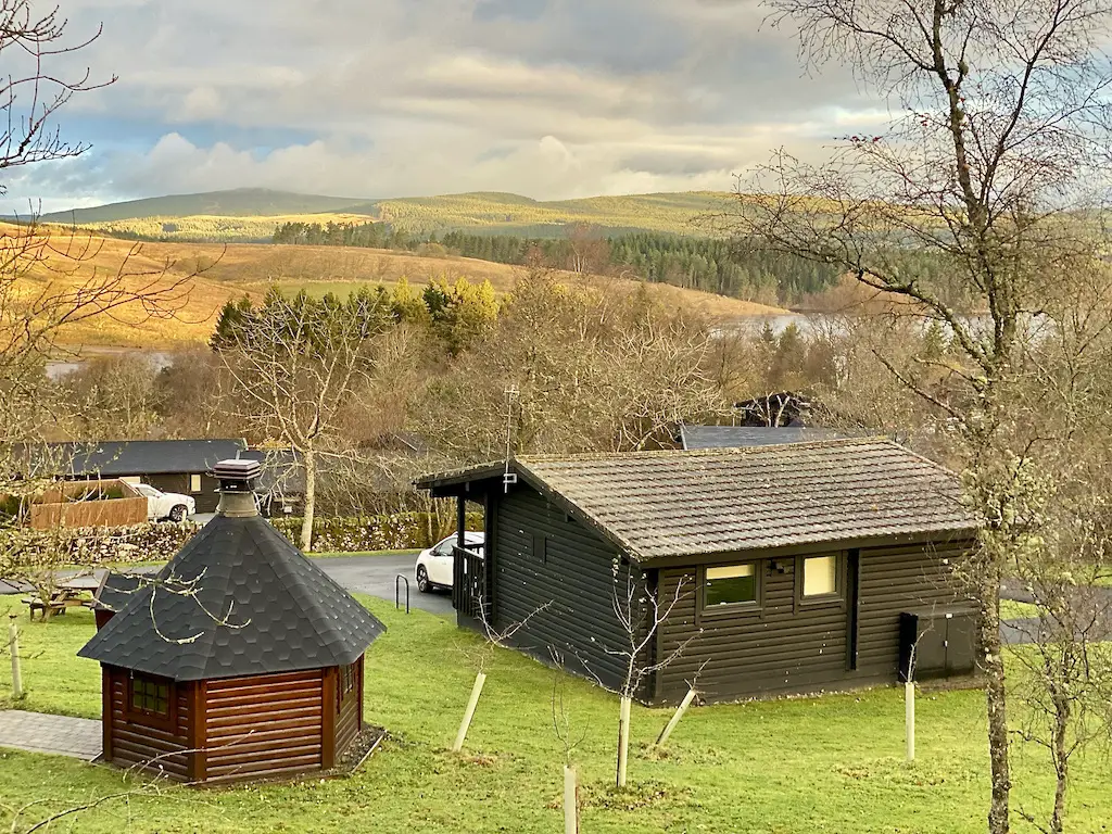 A view of hills and a lake and some wooden lodges. 