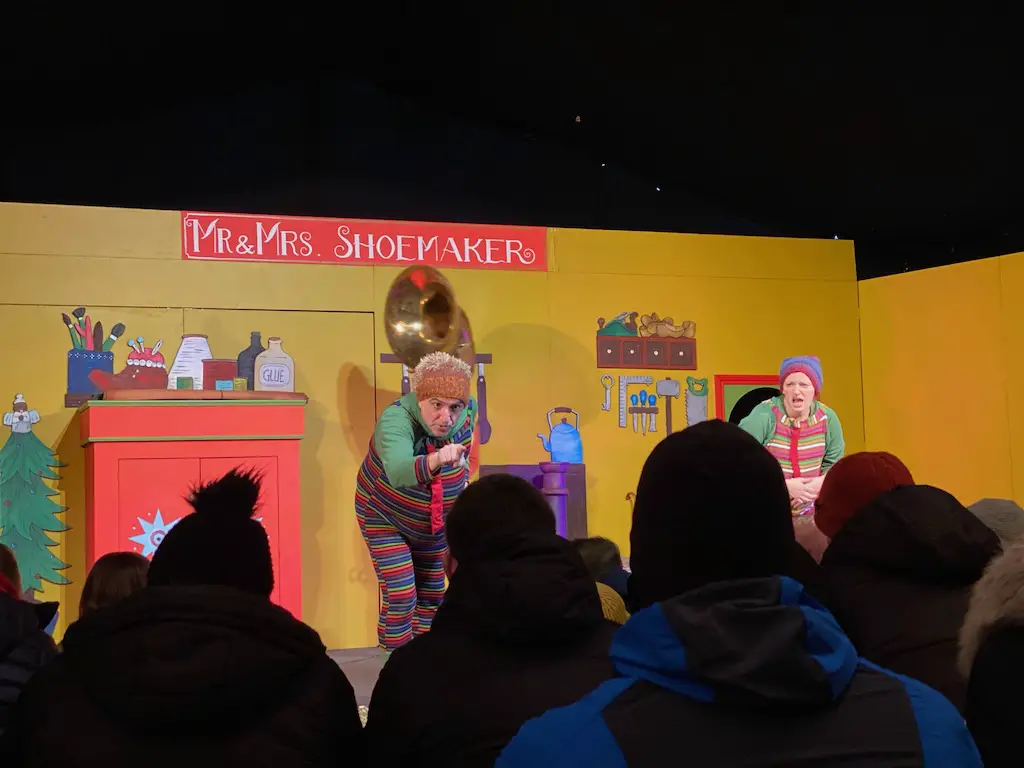 2 people dressed as elves perform on a stage with a back drop that says Mr and Mrs Shoemaker 