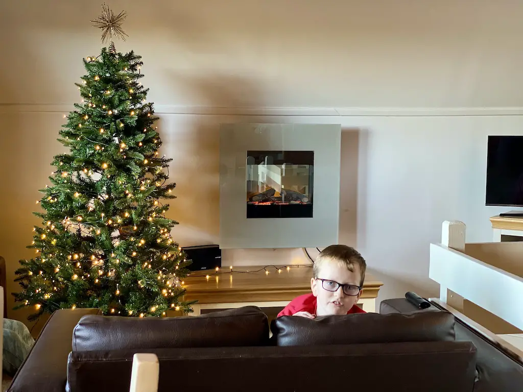 A little boy looks over a sofa with a Christmas tree in the background. 