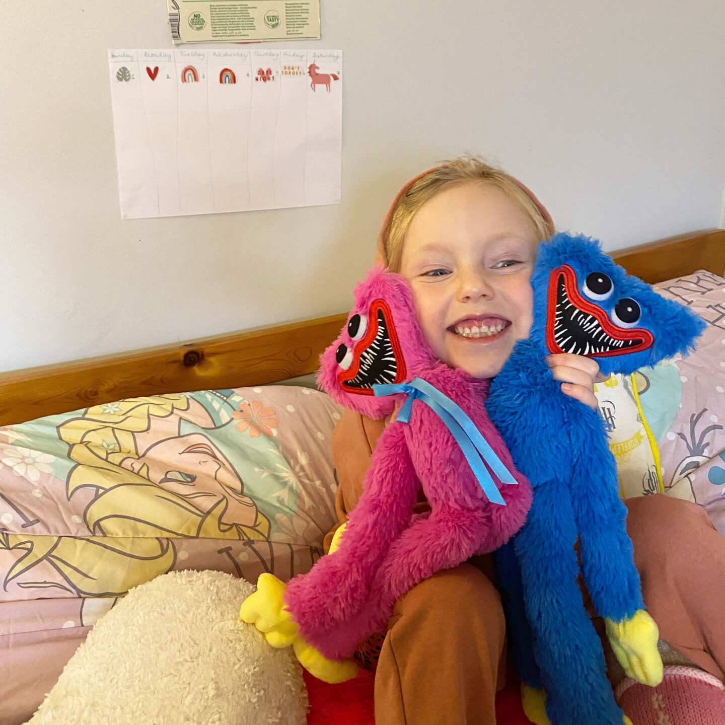 A little girl with a big grin holds up 2 stuffed toys with big smiles and big pointy teeth