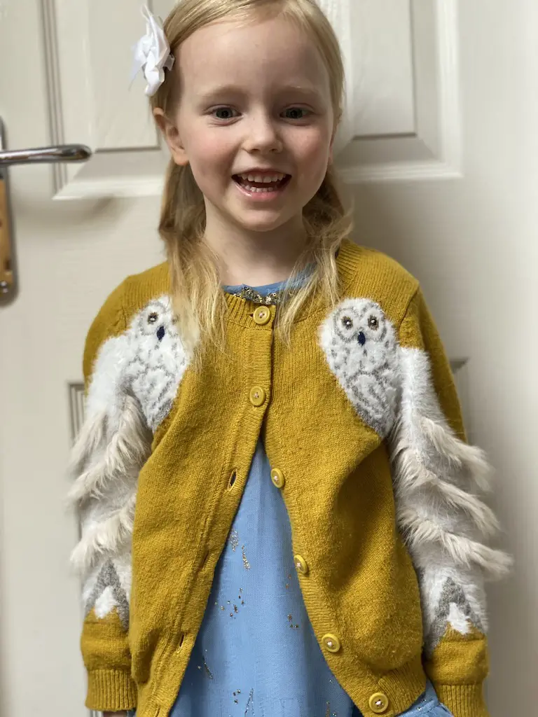 A blonde girl wearing a mustard hedwig harry potter cardigan smiles 