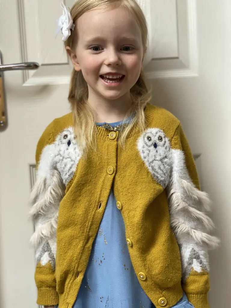 A blonde girl wearing a mustard hedwig harry potter cardigan smiles