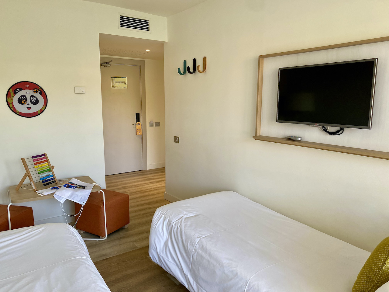 2 single beds, hooks on. a wall and a flatscreen tv