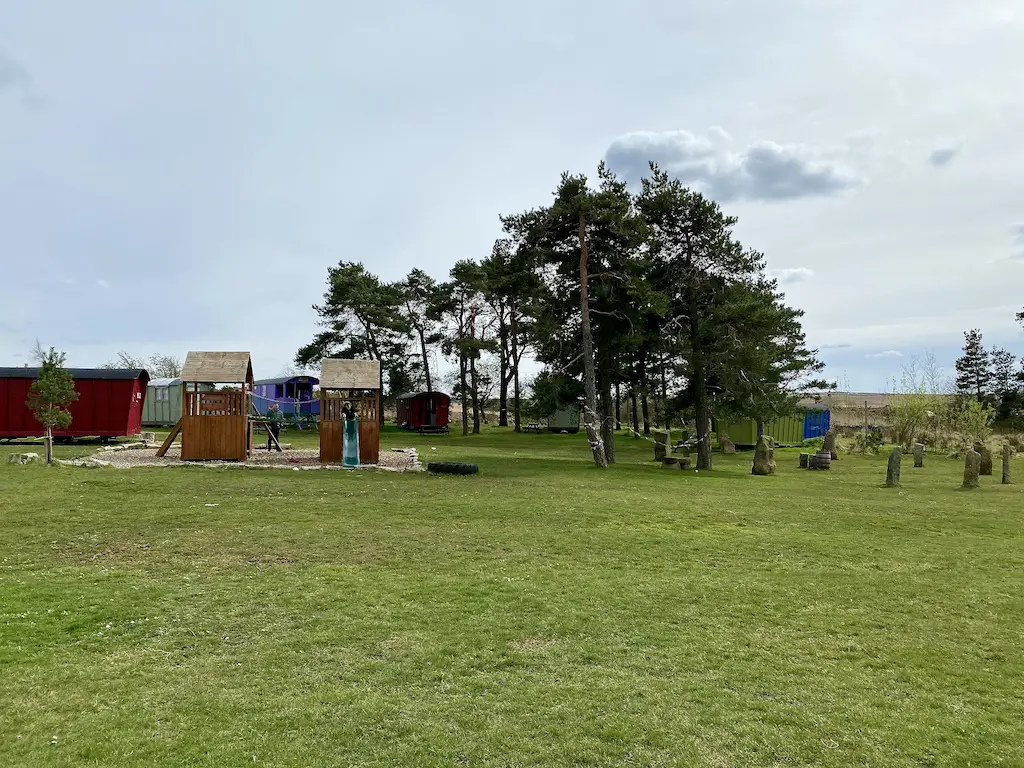 A children's wooden playground and a green field with a stone circle