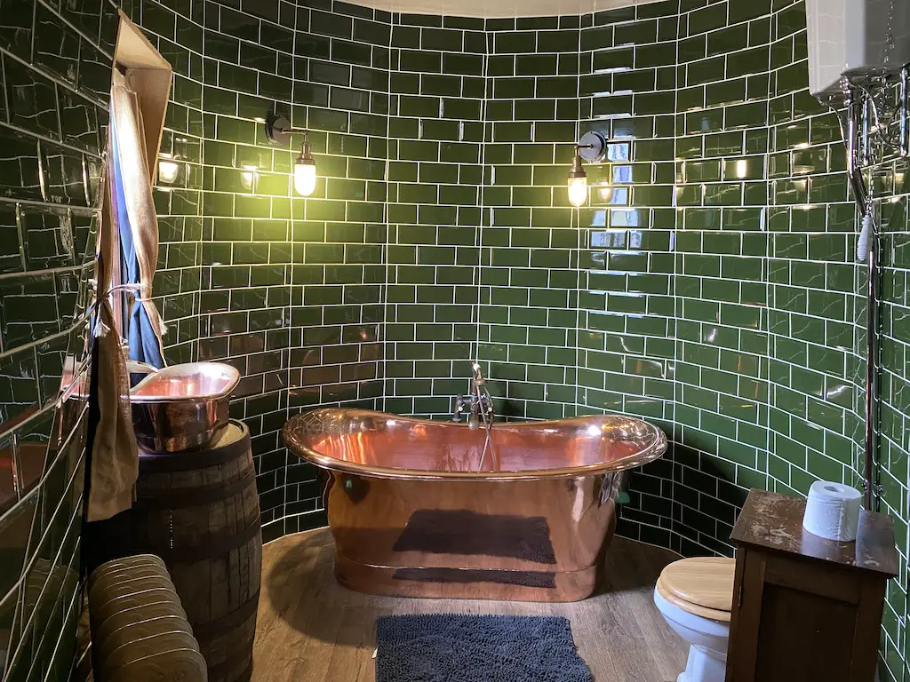 Bathroom with a copper bathtub and green tiles 