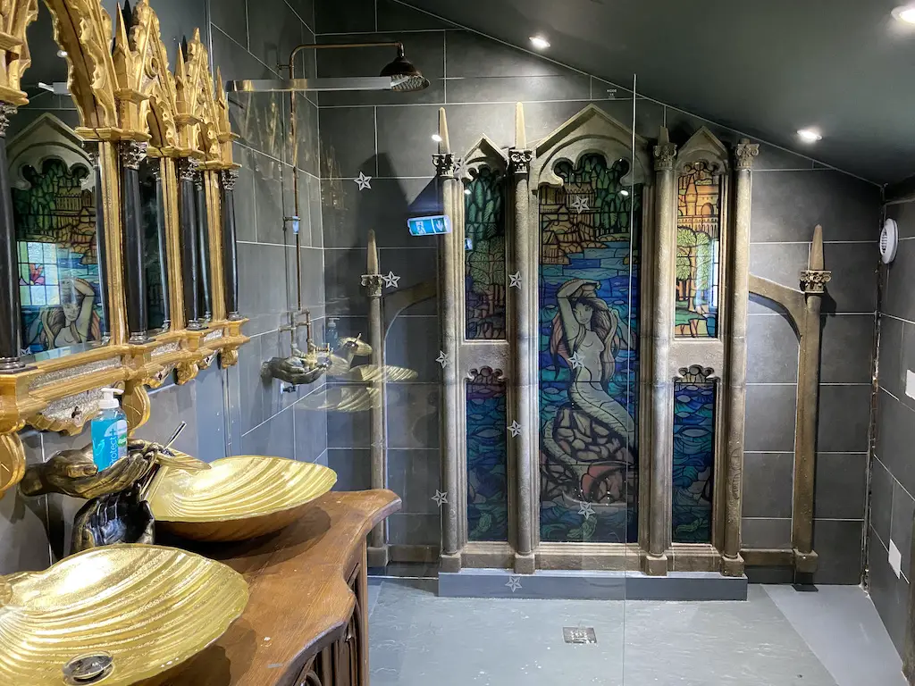 2 gold sinks and shower with a mermaid mosaic to look like the Harry Potter bathrooms
