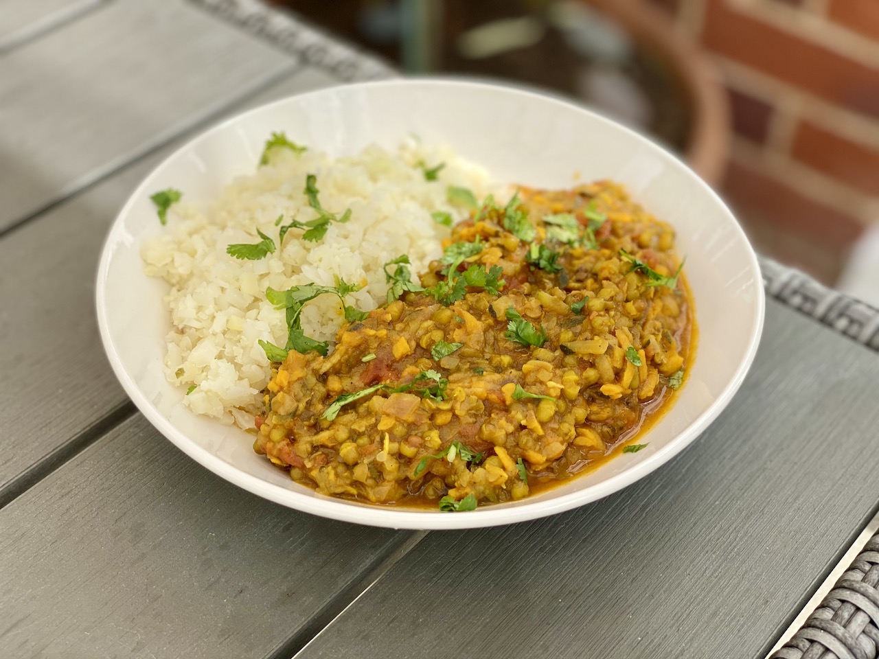 Bowl of mung bean and sweet potato dal on a table with cauliflower rice and coriander