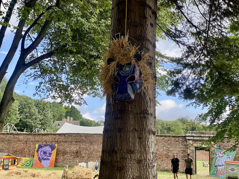 A tree with a large blue lion mask hanging from it with hay for the mane. 