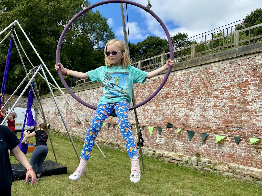 A blonde girl wearing blue rainbow leggings bits in an aerial hoop at a Circus Central at Little Lindi 2022. 