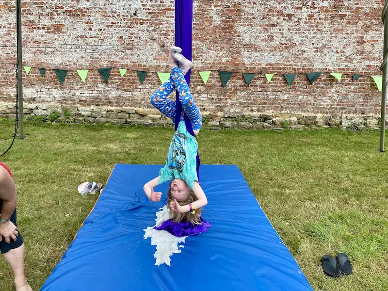 A little blonde girl hangs upside down on silks at a Circus Central workshop at Little Lindi Festival 2022. 