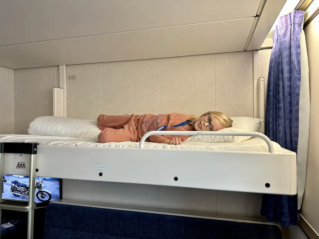 Blonde girl lays on the top bunk of a commodore cabin on a DFDS ferry 