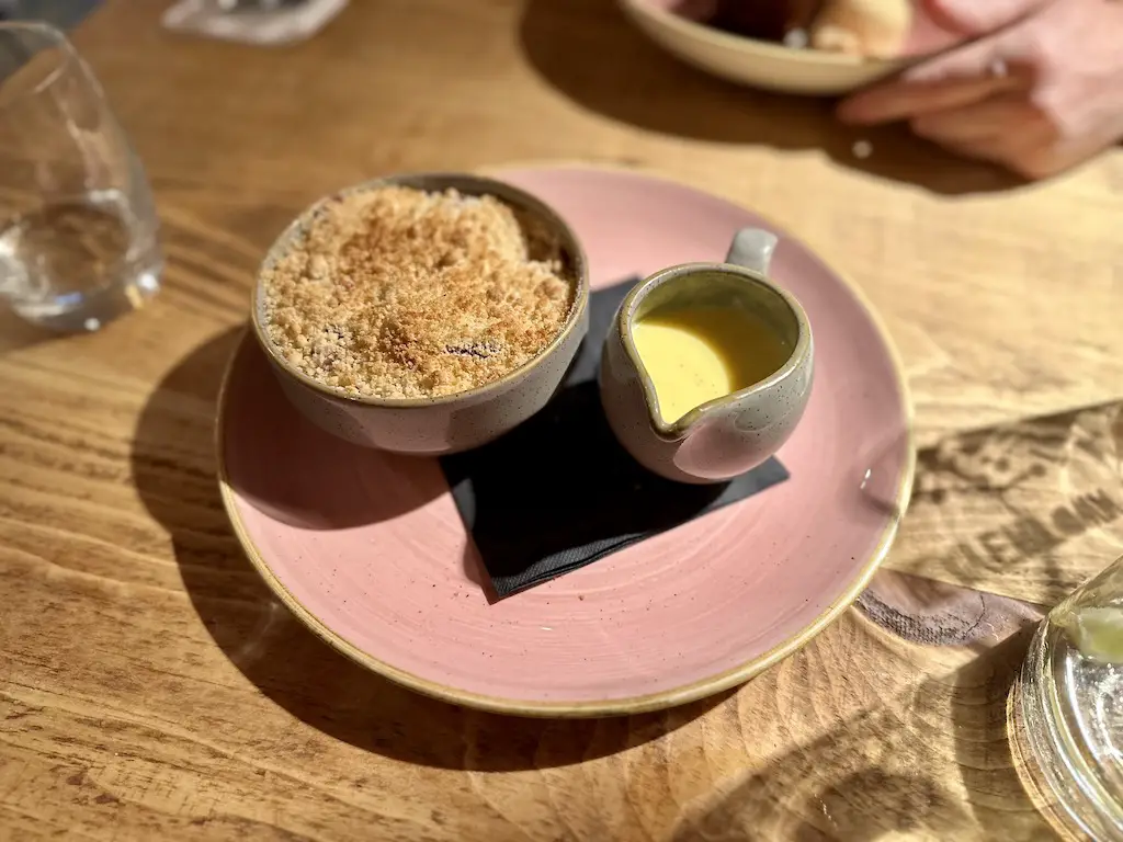Fruit crumble and custard on a pink glazed plate at the Smithy restaurant at Runa Farm