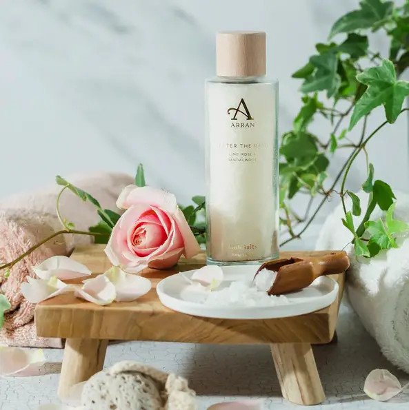 Bath salts on a small wooden table surrounded by roses and petals