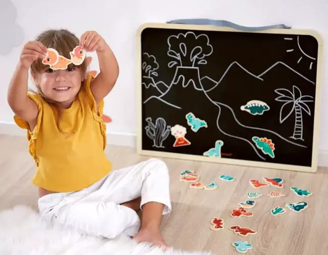 A child plays with a black chalk board and wooden dinosaur magnets with a chalk drawing
